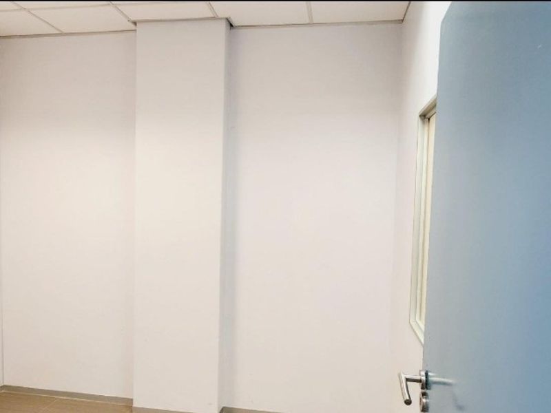 A vacant office space featuring a suspended ceiling, neutral walls, and a standard internal door, providing a clean and functional workspace.