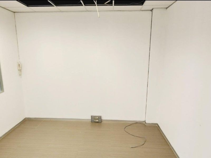 An empty office space featuring a suspended ceiling grid with missing tiles, tiled flooring, and an internal window.
