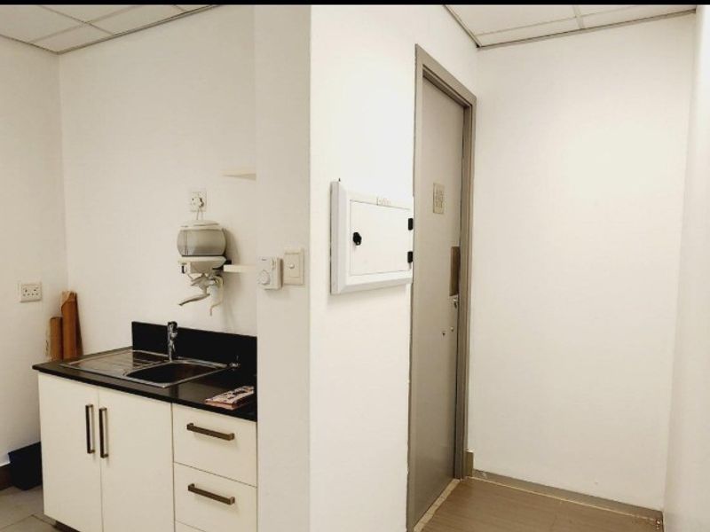 A compact office kitchenette featuring built-in cabinetry, a stainless steel sink, and a drop ceiling, providing essential utility space for the office environment.