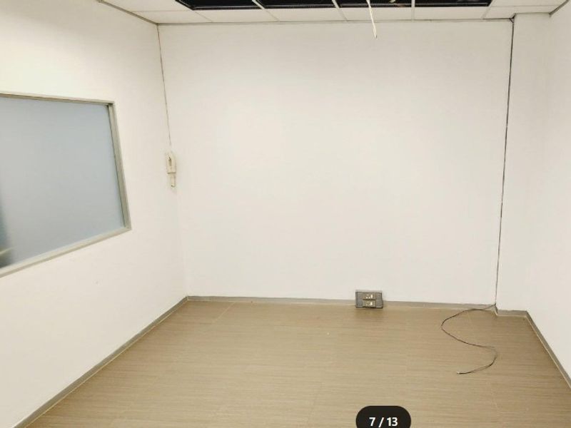 An empty office space featuring laminate flooring, a frosted glass partition, and a suspended ceiling with some missing tiles and exposed wiring.