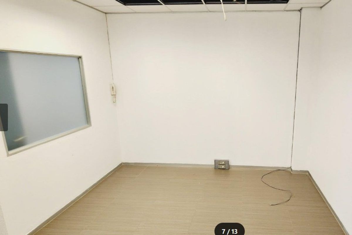 An empty office space featuring laminate flooring, a frosted glass partition, and a suspended ceiling with some missing tiles and exposed wiring.