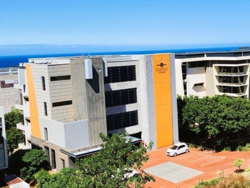 Aerial view of a modern multi-story office building featuring a distinctive orange accent facade, paved parking area, and surrounding landscaped grounds.