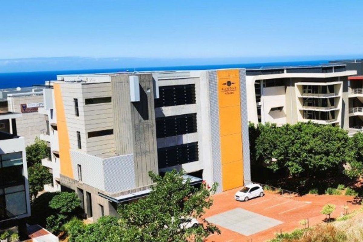 Aerial view of a modern multi-story office building featuring a distinctive orange accent facade, paved parking area, and surrounding landscaped grounds.