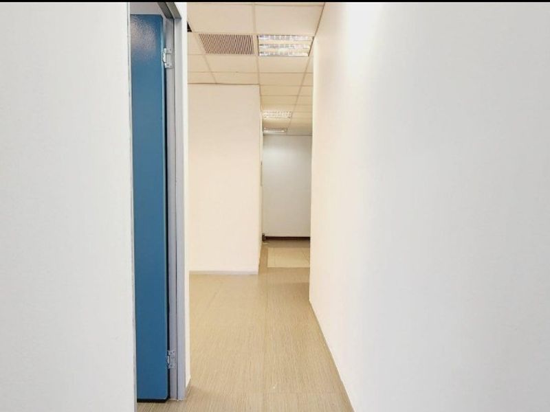 A clean, empty office hallway featuring neutral walls, laminate flooring, and a suspended ceiling with integrated lighting and ventilation.