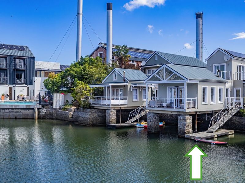 Waterfront residential property featuring elevated structures on stone-clad stilts, private jetties, and direct water access in a scenic estate setting.