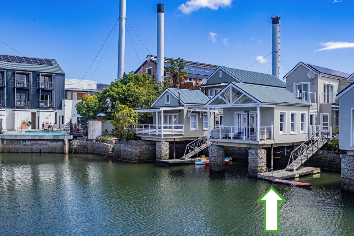 Waterfront residential property featuring elevated structures on stone-clad stilts, private jetties, and direct water access in a scenic estate setting.