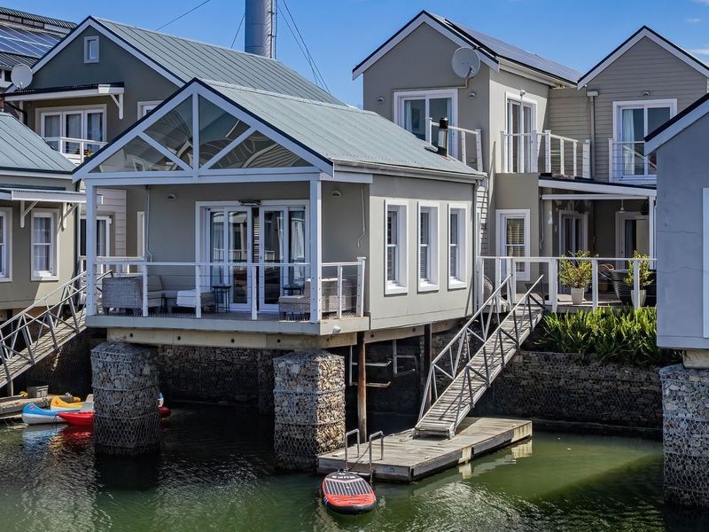Rear view of a waterfront property featuring a raised deck, private jetty, and direct water access with modern architectural finishes.