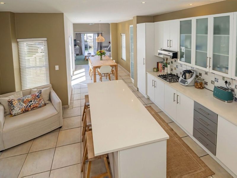 Spacious open-plan kitchen and dining area featuring a central island, modern cabinetry, gas hob, and tiled flooring with direct access to the outdoor space.