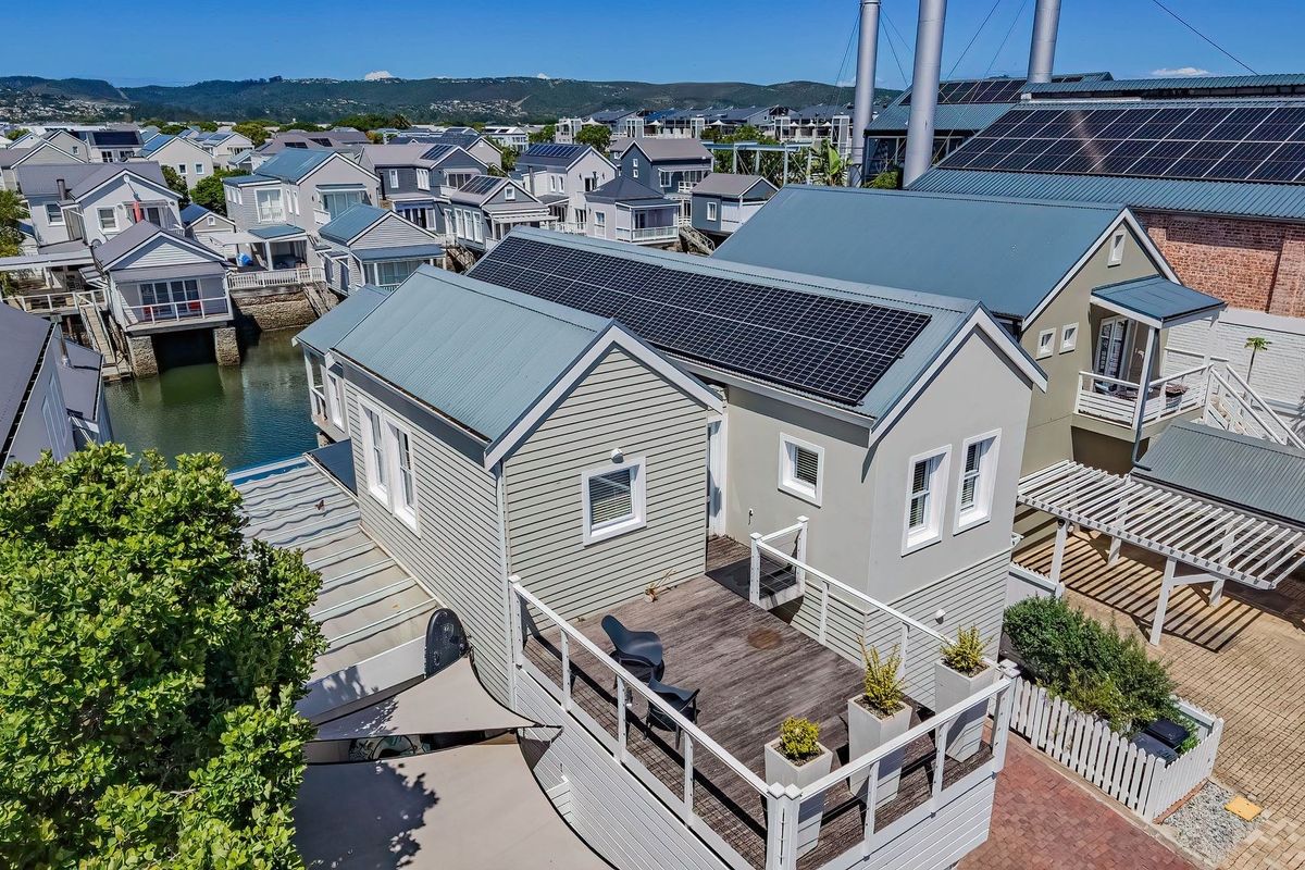 Aerial view of a residential property featuring a metal roof with integrated solar panels, a timber deck, and a well-maintained exterior in a waterfront estate.