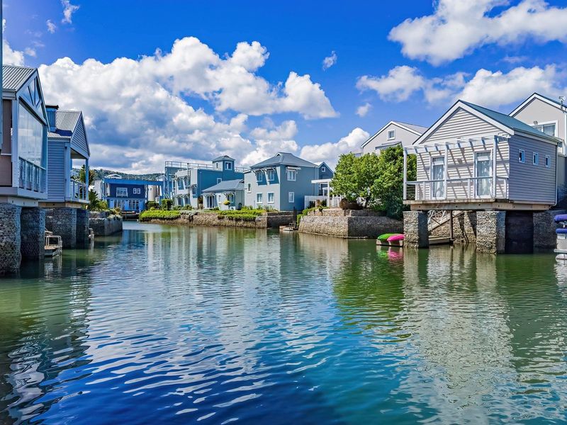 A scenic view of a waterfront residential estate featuring well-maintained homes with private jetties and stone retaining walls along the canal.