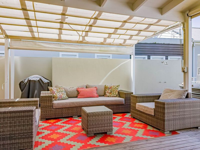 A covered outdoor patio featuring timber decking, a retractable fabric awning, and a private boundary wall with an integrated outdoor shower.