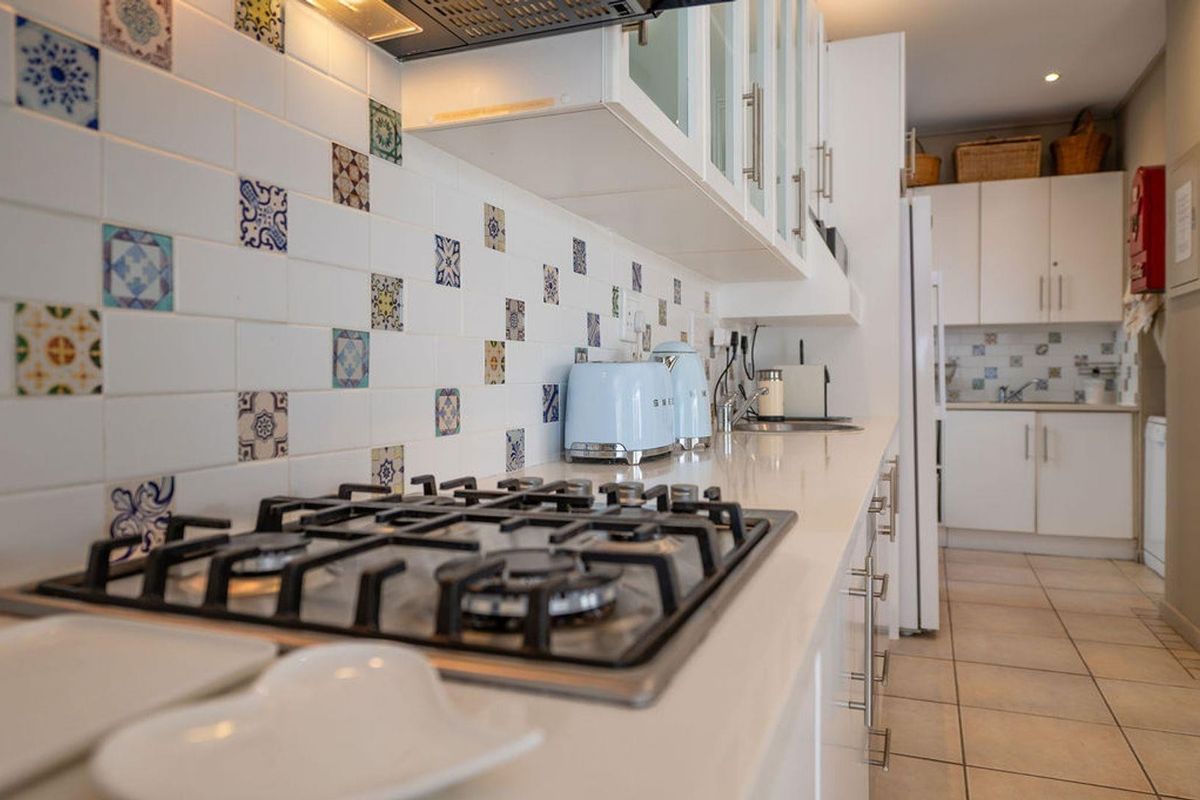 A well-maintained kitchen featuring a gas hob, decorative tiled backsplash, quartz countertops, and ample built-in cabinetry with a clean, functional layout.