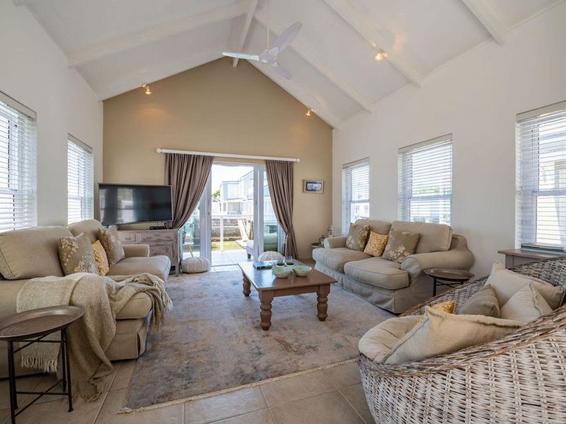 Spacious living room featuring a high vaulted ceiling, ceiling fan, tiled flooring, and large sliding glass doors providing access to the outdoor patio area.
