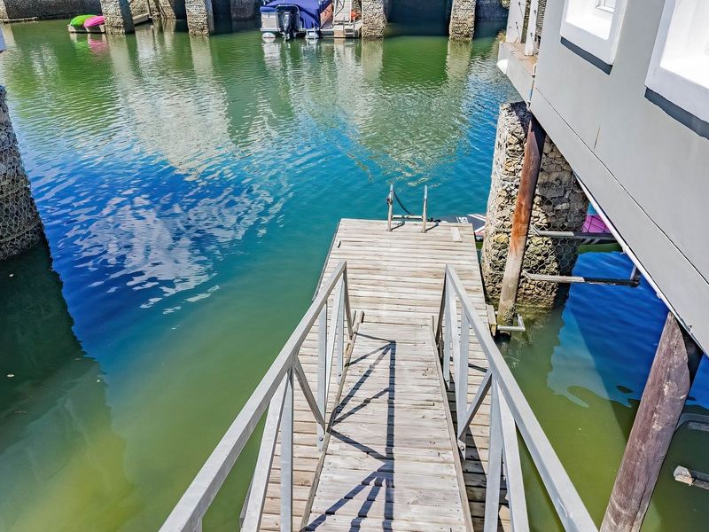 A private wooden jetty extending over the water, featuring metal handrails and stone-filled gabion support pillars for direct water access.