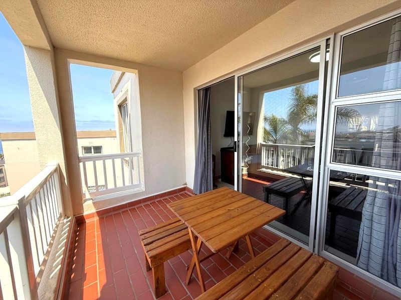 A covered balcony featuring tiled flooring and sliding glass door access, providing an outdoor space with views of the surrounding area.