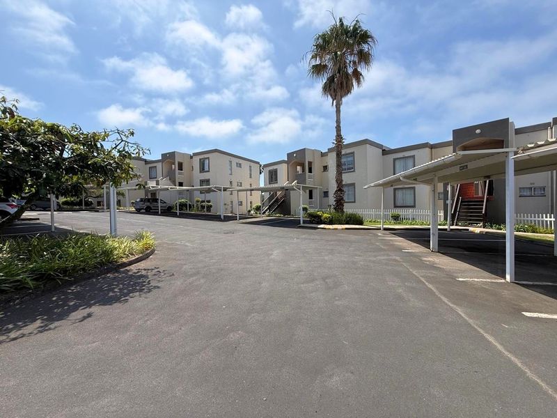 Exterior view of an apartment complex featuring paved parking areas with covered carports and multi-story residential buildings.
