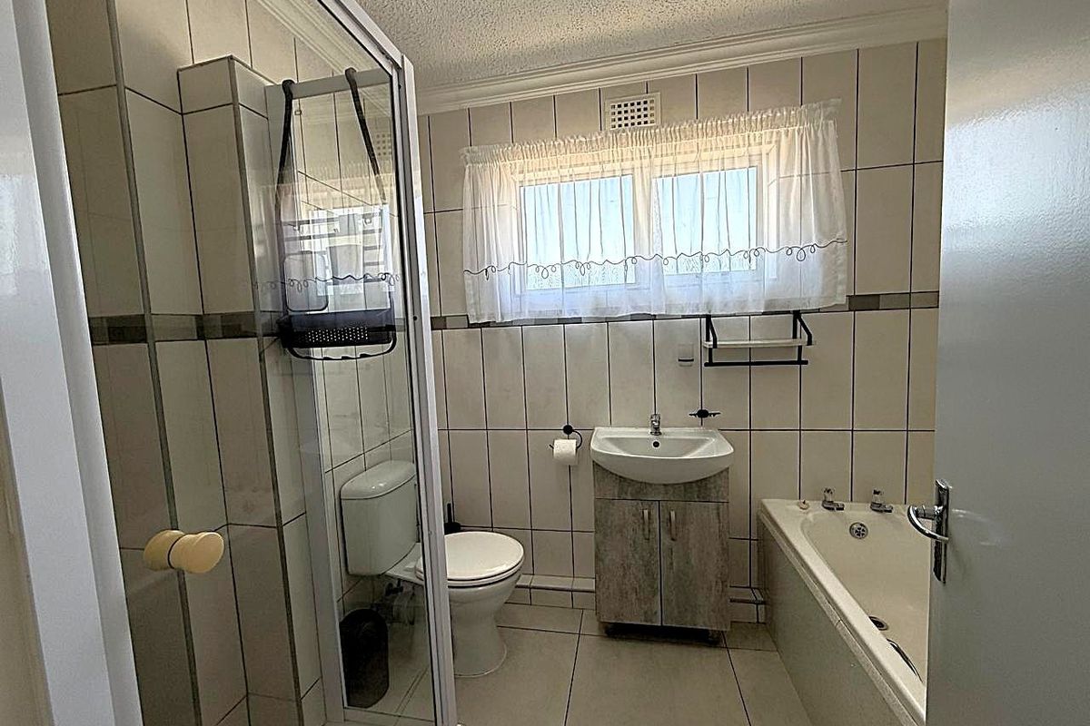 A functional bathroom featuring a shower enclosure, bathtub, vanity cabinet with washbasin, and tiled finishes throughout.