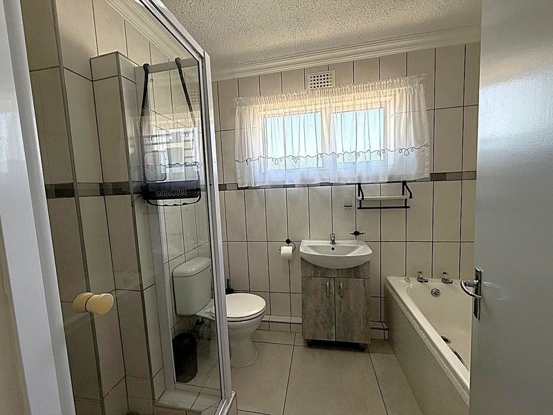 A functional bathroom featuring a shower enclosure, bathtub, vanity cabinet with washbasin, and tiled finishes throughout.