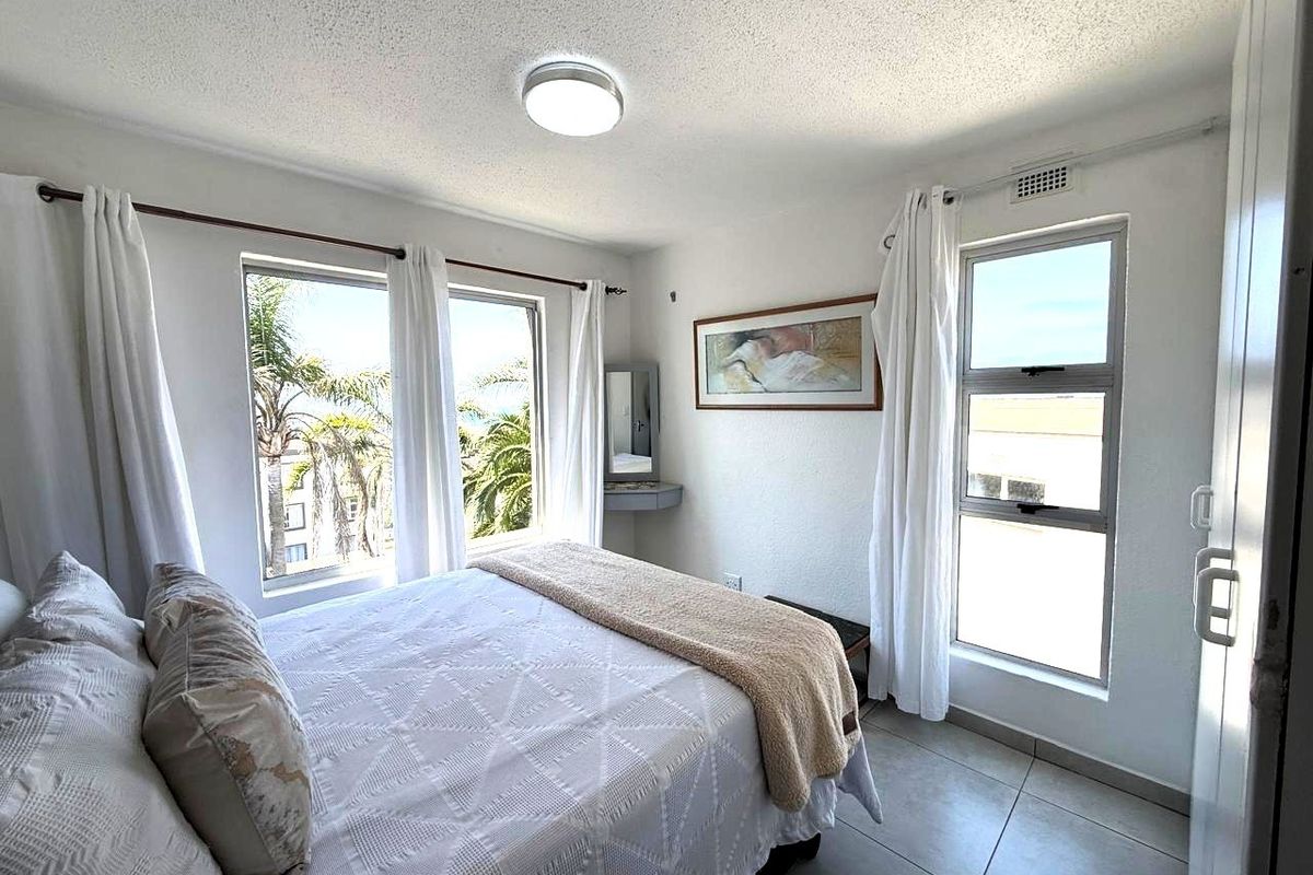 A bright bedroom featuring tiled flooring, large windows with natural light, and a built-in vanity unit.