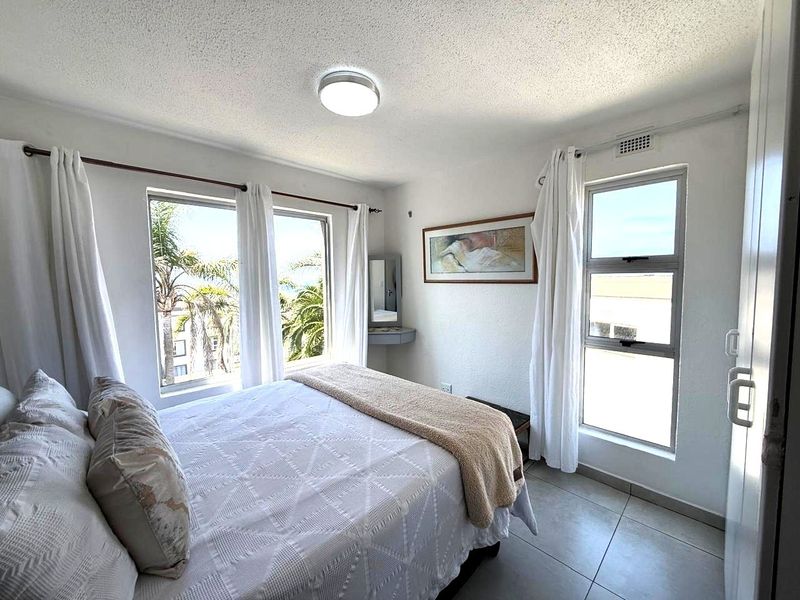 A bright bedroom featuring tiled flooring, large windows with natural light, and a built-in vanity unit.
