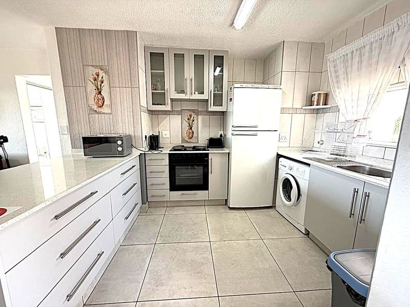 A functional kitchen featuring white cabinetry, stone countertops, tiled flooring, and integrated appliances, offering a clean and practical workspace.