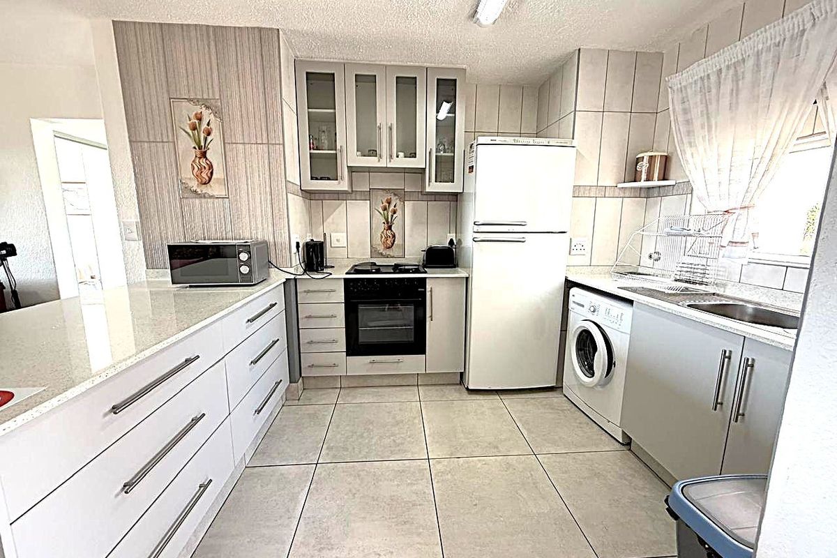 A functional kitchen featuring white cabinetry, stone countertops, tiled flooring, and integrated appliances, offering a clean and practical workspace.