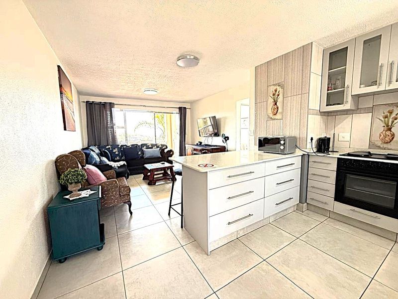 Open-plan living area featuring a modern kitchen with a central island, built-in oven, and tiled flooring, seamlessly connecting to the lounge space.