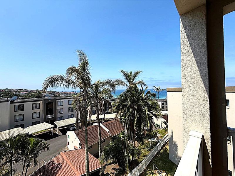 A balcony view overlooking the apartment complex grounds, parking area, and distant ocean horizon.