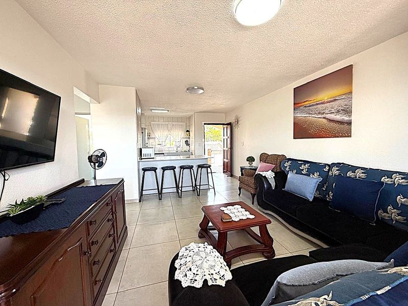 An open-plan living and kitchen area featuring tiled flooring, a breakfast bar, and direct access to an exterior doorway.