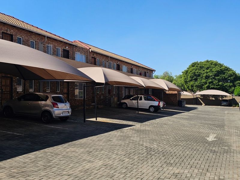 Exterior view of a townhouse complex featuring a paved parking area with multiple shade cloth carports and brick building facades.