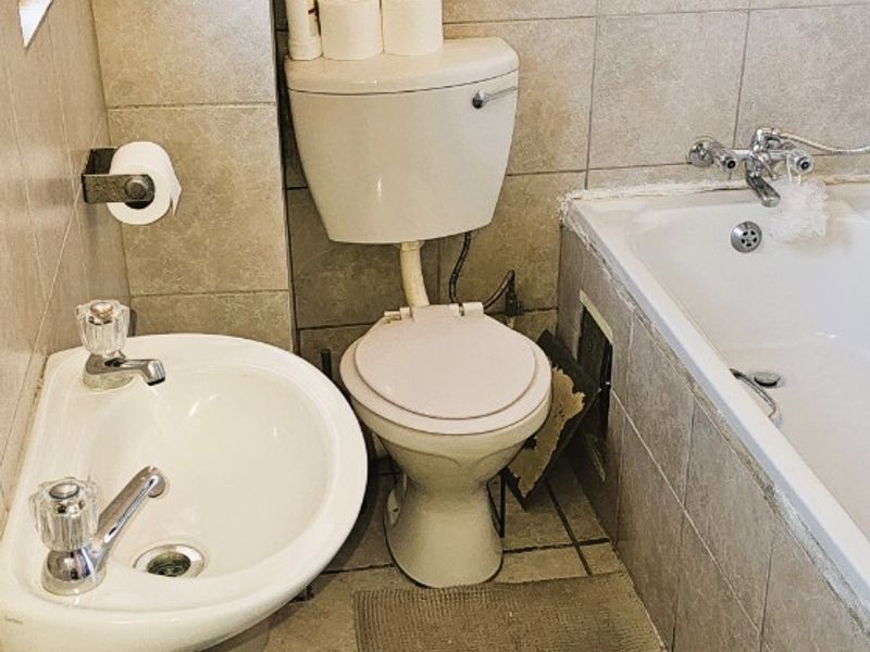 A compact bathroom featuring a pedestal basin, toilet, and bathtub with tiled finishes, currently requiring maintenance and cosmetic updates.