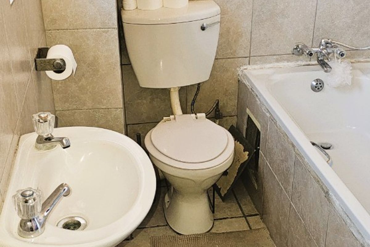 A compact bathroom featuring a pedestal basin, toilet, and bathtub with tiled finishes, currently requiring maintenance and cosmetic updates.