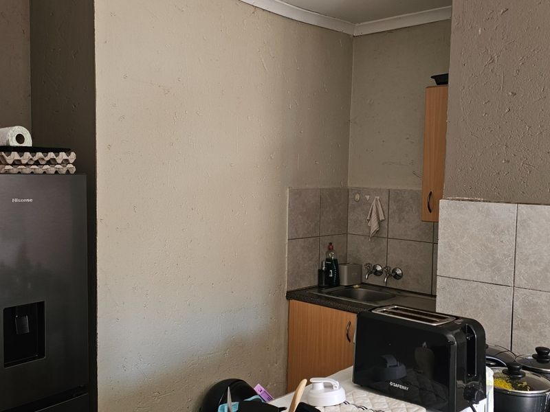 A compact kitchen area featuring built-in cabinetry, a stainless steel sink, and tiled splashback, requiring cosmetic updates to improve the overall aesthetic.