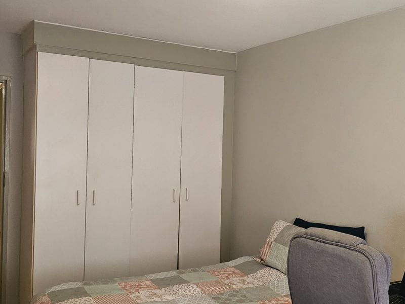 A bedroom featuring built-in cupboards with a view into the adjacent kitchen area.