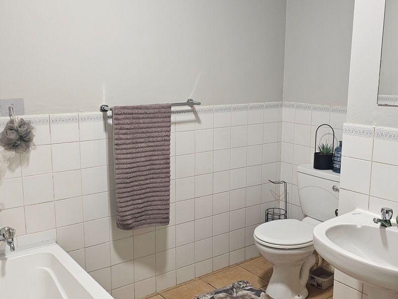 A functional bathroom featuring a bathtub, pedestal basin, and toilet with classic white wall tiling and neutral floor tiles.