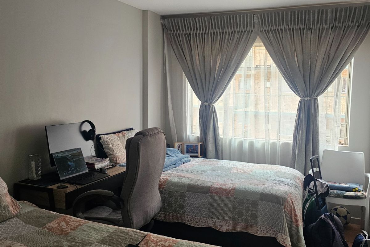 A functional bedroom featuring a window with installed curtain tracks, providing natural light and a view of the surrounding building exterior.