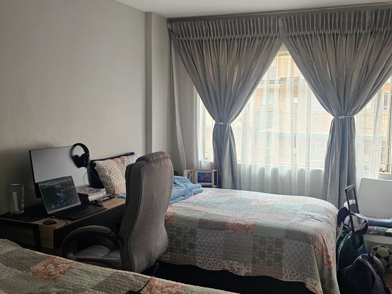 A functional bedroom featuring a window with installed curtain tracks, providing natural light and a view of the surrounding building exterior.