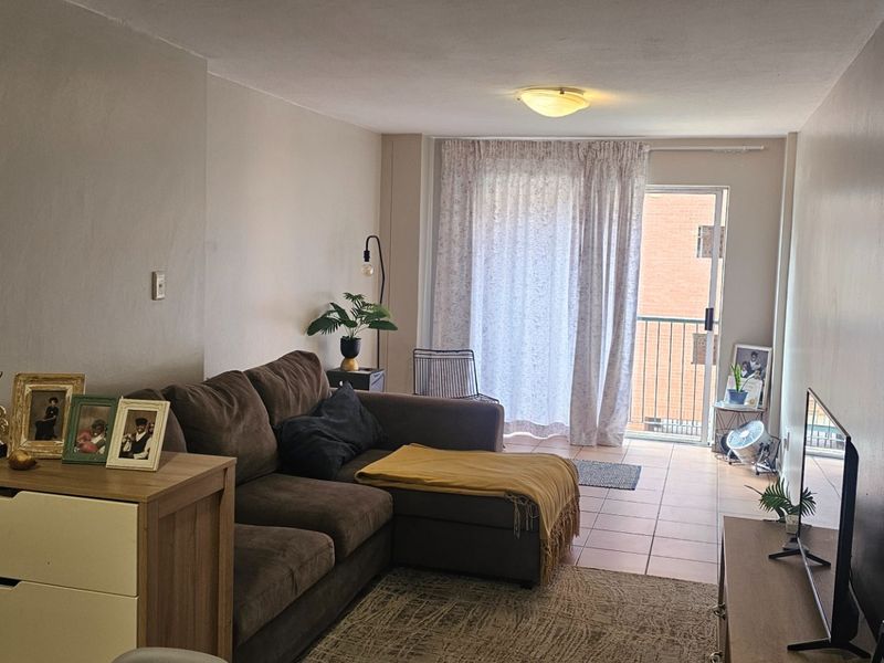 A living room area featuring tiled flooring and a sliding glass door providing access to a balcony, offering natural light and outdoor connectivity.