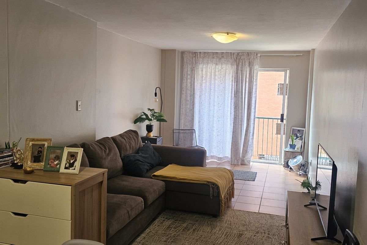 A living room area featuring tiled flooring and a sliding glass door providing access to a balcony, offering natural light and outdoor connectivity.
