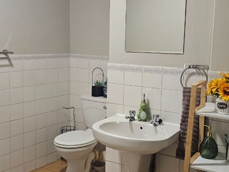 A functional bathroom featuring a pedestal washbasin, toilet, wall-mounted mirror, and extractor fan, finished with ceramic wall and floor tiling.