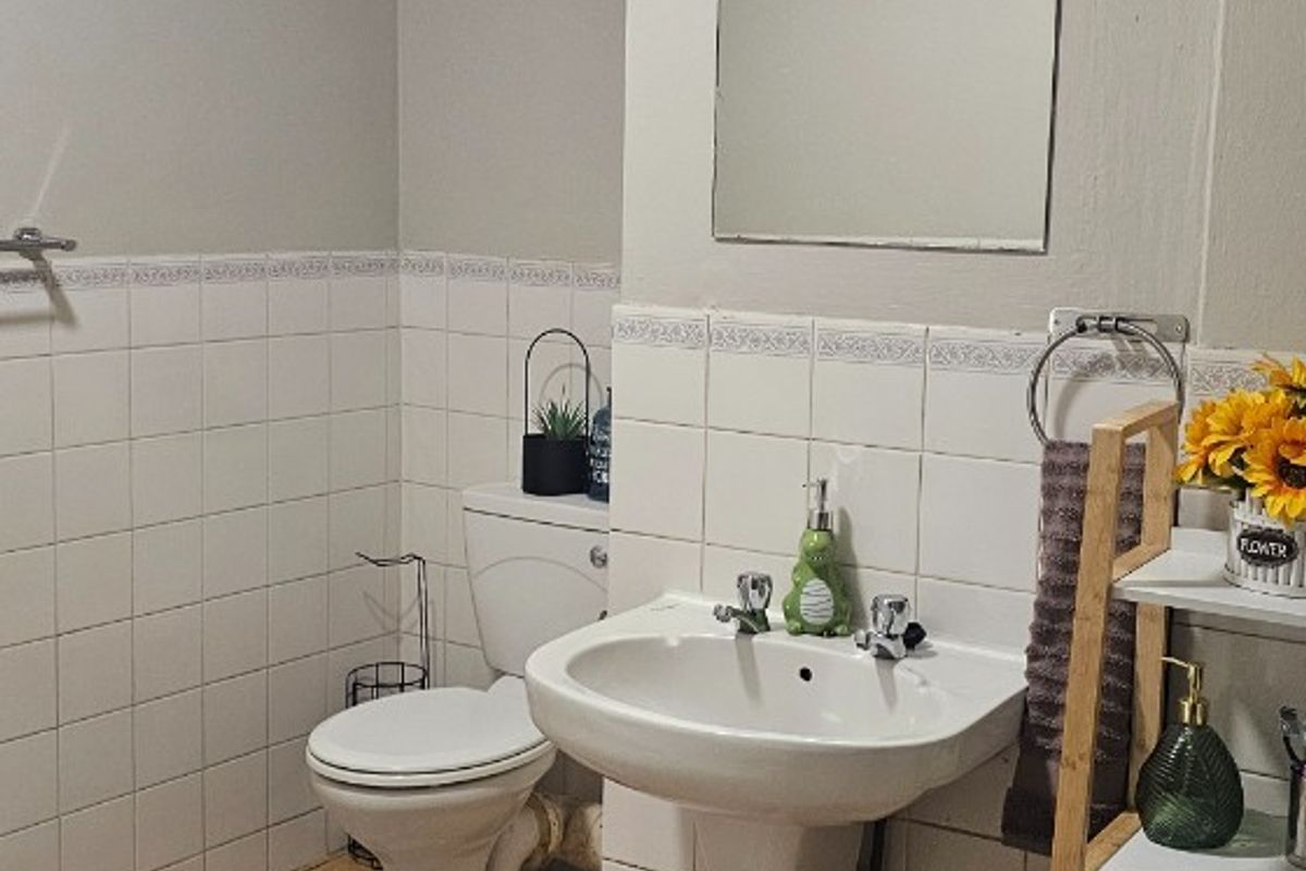 A functional bathroom featuring a pedestal washbasin, toilet, wall-mounted mirror, and extractor fan, finished with ceramic wall and floor tiling.