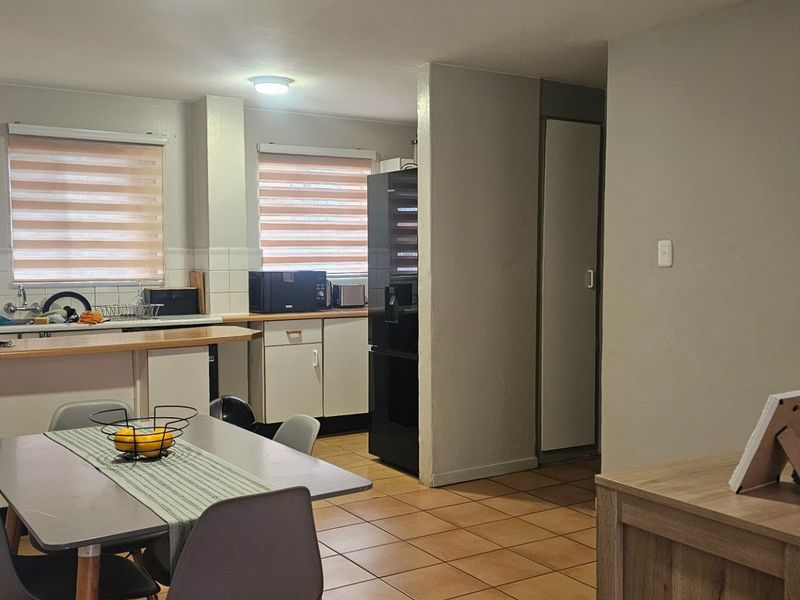 Open plan kitchen and dining area featuring tiled flooring, built-in cabinetry, and direct access to an exterior area through a security gate.