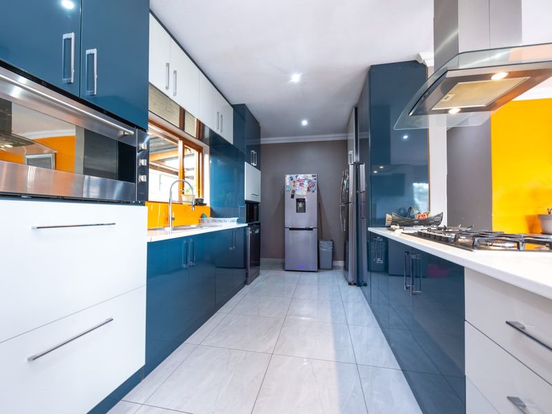 Modern galley-style kitchen featuring high-gloss blue and white cabinetry, stone countertops, integrated appliances, and sleek tiled flooring.