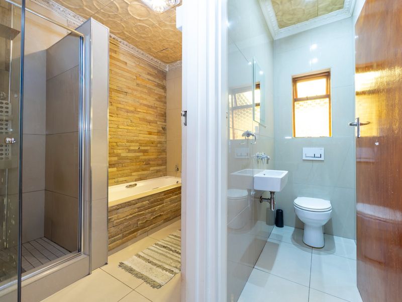 Modern bathroom featuring a glass shower enclosure, built-in bathtub with stone cladding, wall-mounted basin, and wall-hung toilet with tiled finishes.