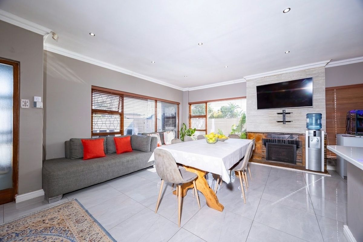 Spacious open-plan living and dining area featuring tiled floors, recessed lighting, and a prominent stone-clad fireplace as a central focal point.