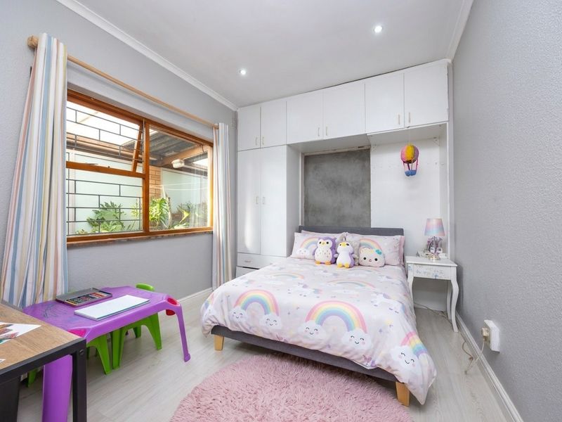 A well-lit bedroom featuring built-in white cupboards, light-toned flooring, and a large window with security bars, offering a clean and functional living space.