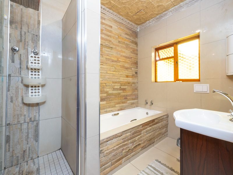 Modern bathroom featuring a glass-enclosed shower, a built-in bathtub with stone cladding, and a vanity basin with contemporary fixtures.