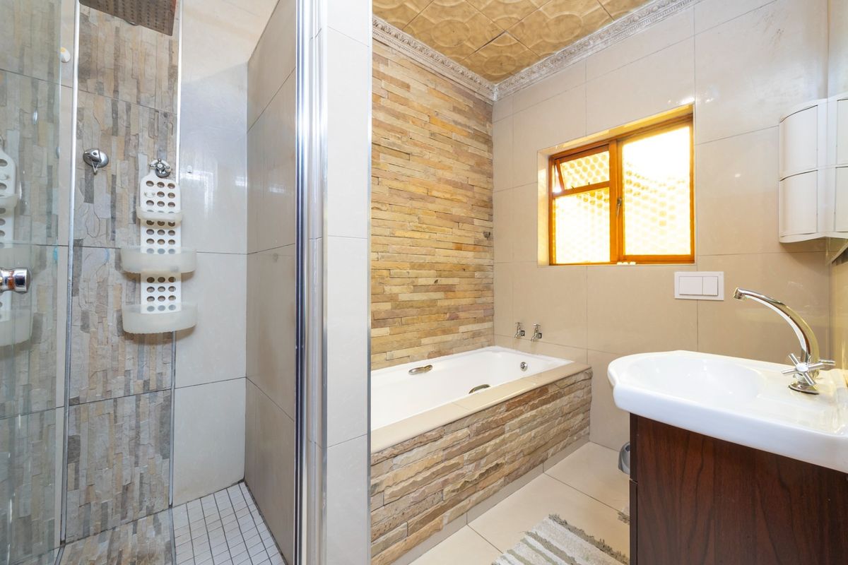 Modern bathroom featuring a glass-enclosed shower, a built-in bathtub with stone cladding, and a vanity basin with contemporary fixtures.