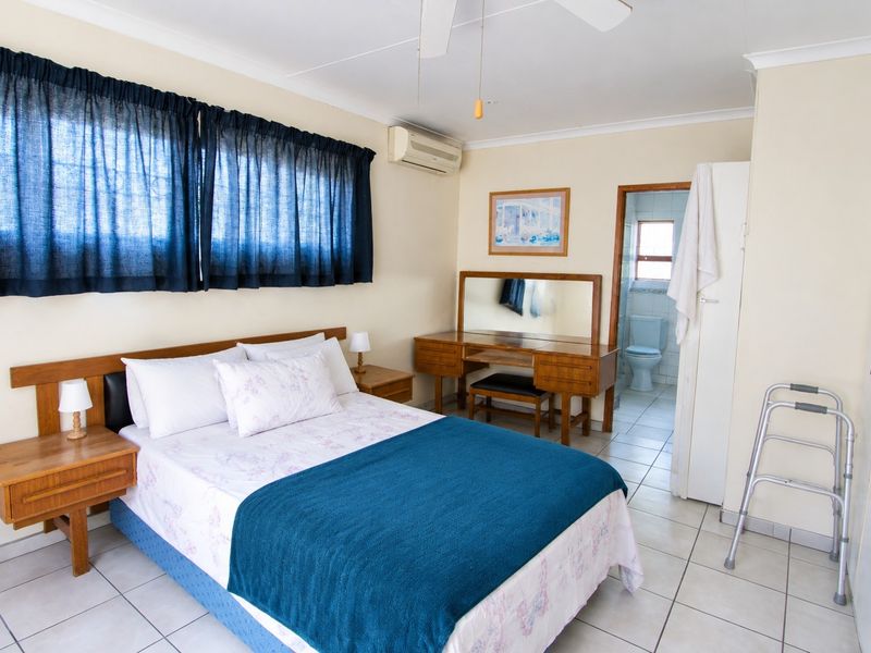 A well-maintained bedroom featuring tiled flooring, a ceiling fan, split-system air conditioning, and convenient access to an en-suite bathroom.