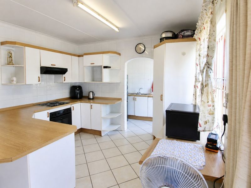 Functional kitchen featuring white cabinetry, laminate countertops, built-in oven and hob, with an adjoining scullery area and tiled flooring throughout.